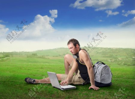 蓝天白云绿野下笔记本上网工作的帅哥图片