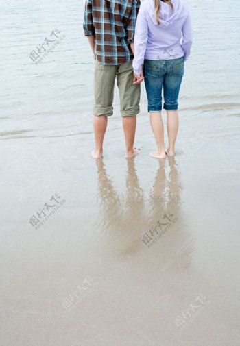海边沙滩手拉手的情侣腿部特写图片
