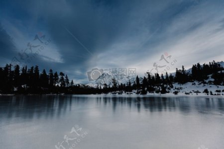 蓝白色多云天空之上半冰冻的湖面景观森林接壤