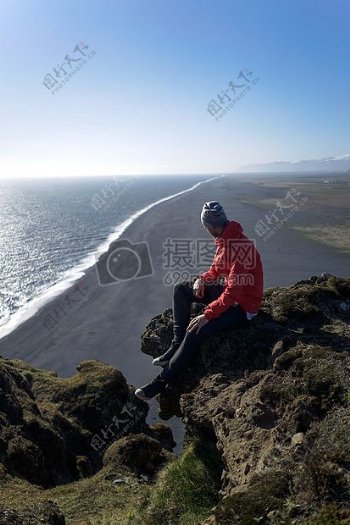 男子在红夹克在白天在海滩上的岩石坐