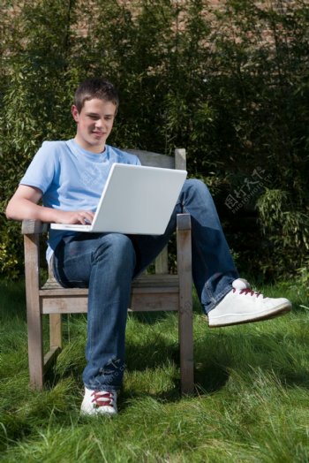 坐在户外椅子上玩电脑的男孩图片
